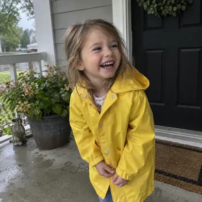AI-generated photo: a laughing four-year-old in a yellow raincoat on a wet front porch.